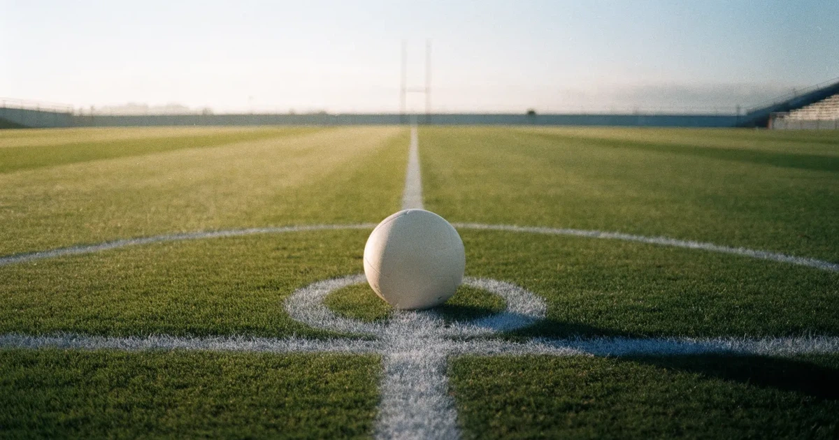 Uma bola de futebol no ponto central de um relvado, à luz da manhã