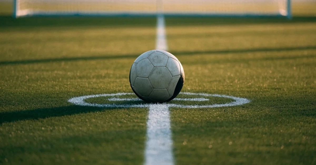 Uma bola de futebol no ponto central de um relvado, à luz da manhã